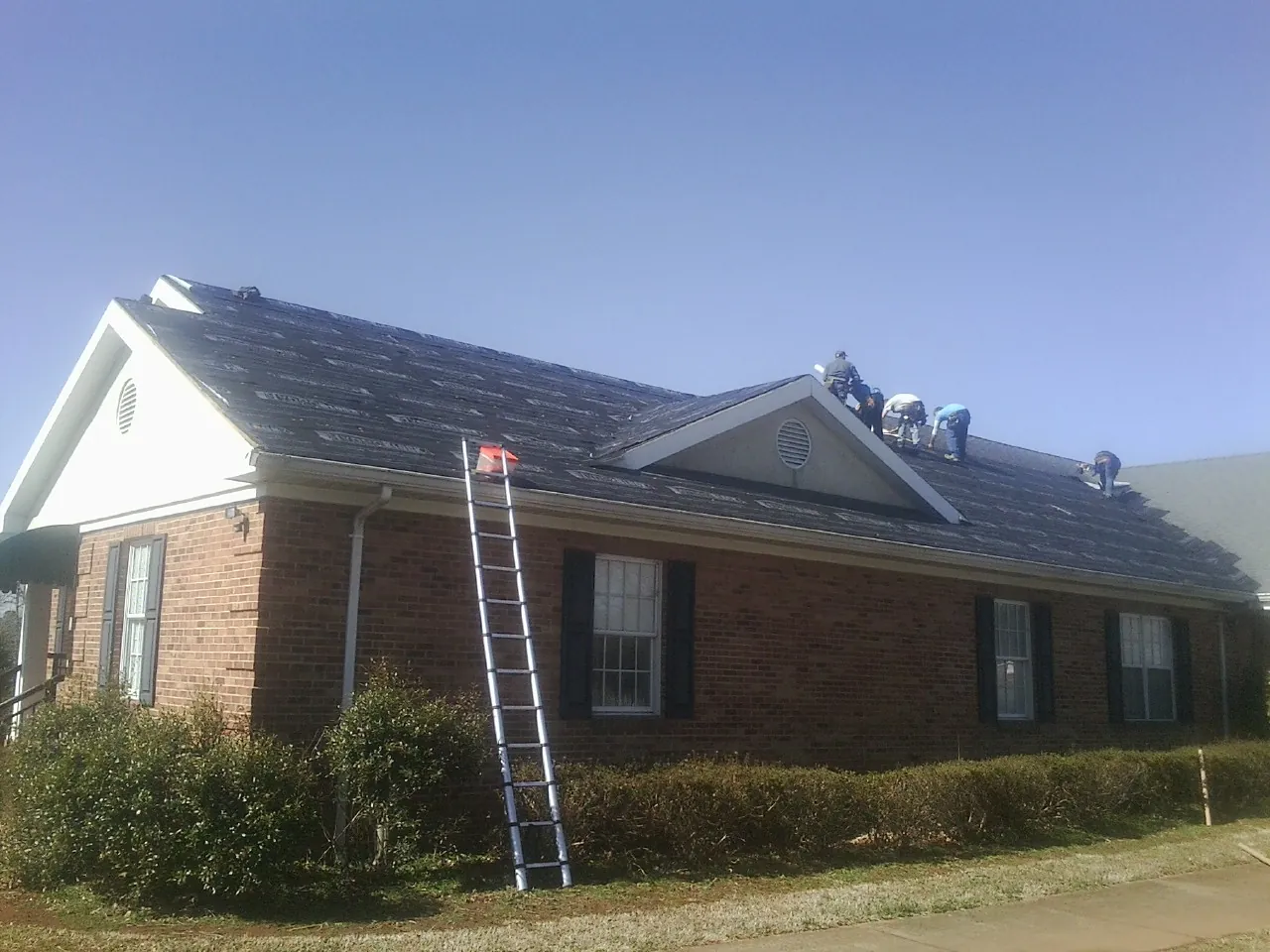 Crew tearing shingles off a brick ranch roof with a ladder set — Metal Roof Repair work by our crew in East Mc Keesport