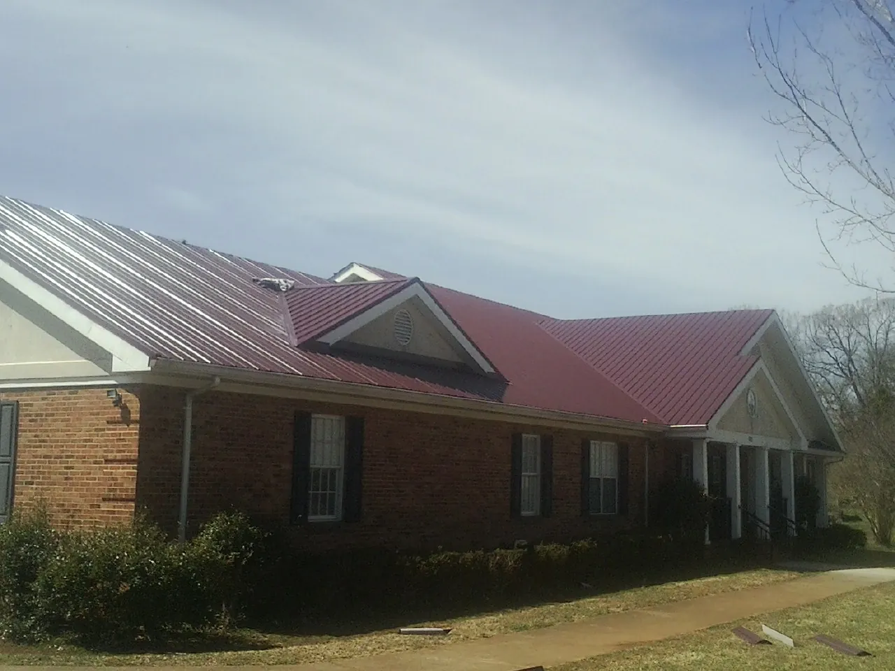 Red metal roof with gabled entries on a long brick building, from a Hail Damage Roof Repair job in East Mc Keesport