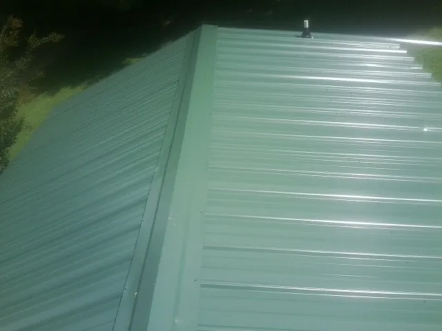 New green metal panels meeting at the ridge of a roof — Flat Roof Repair work by our crew in East Mc Keesport