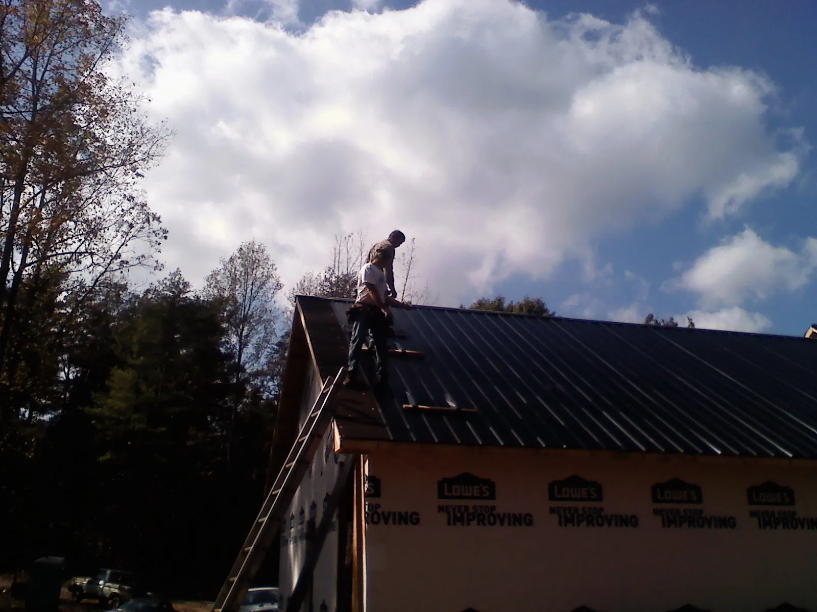 Roofer fastening dark metal panels high against a cloudy sky, from a Roof Inspection job in East Mc Keesport