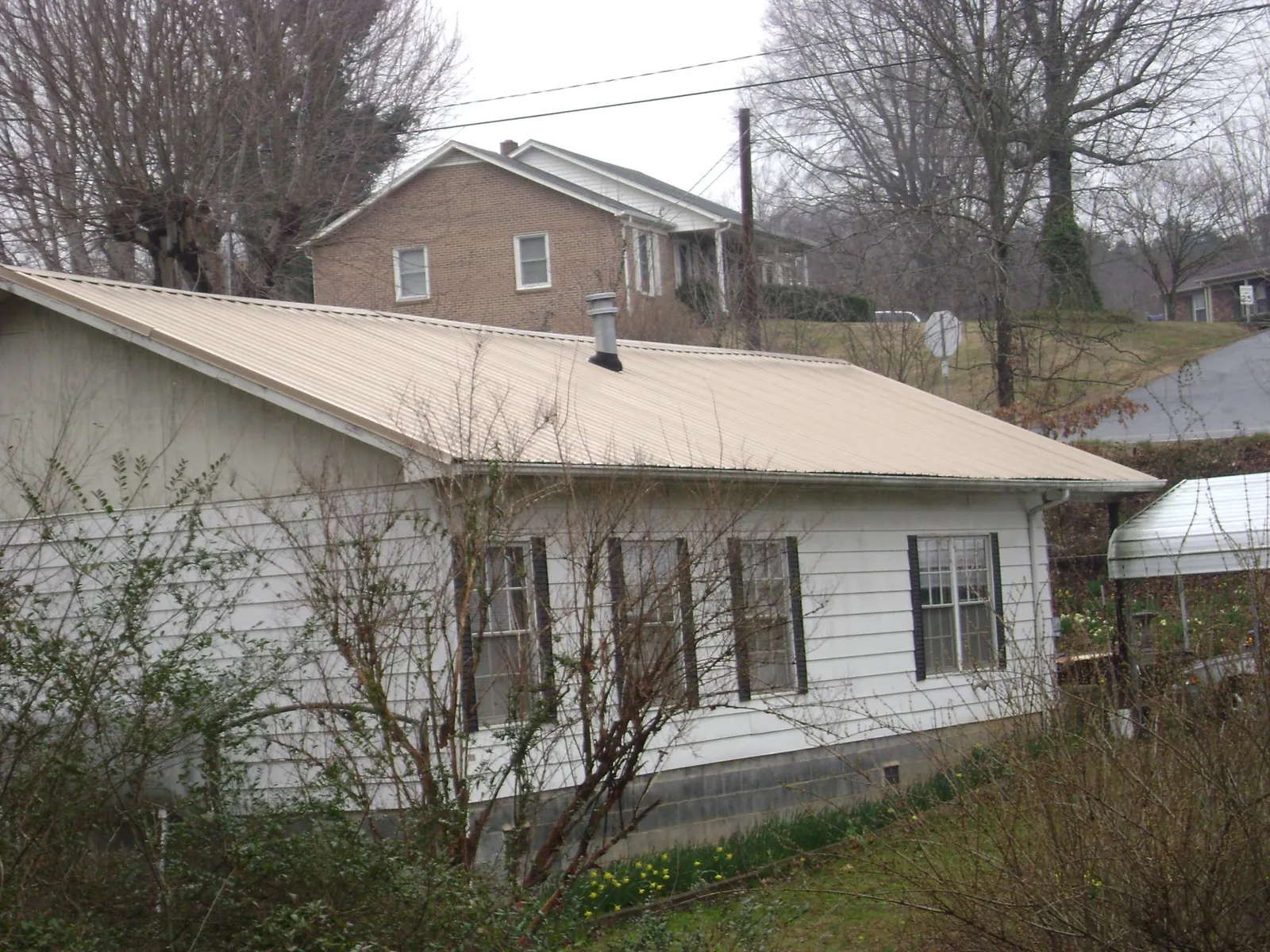Tan metal roof on a white sided house set into a hillside — Commercial Roofing by Roofing Brothers in East Mc Keesport